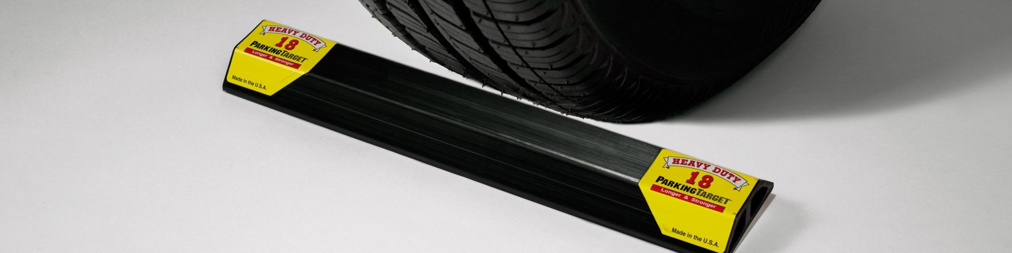A black HD-18 Heavy Duty ParkingTarget lying in front of a vehicle tire, with yellow end caps reading Heavy Duty 18 ParkingTarget, Longer & Stronger, Made in the U.S.A.